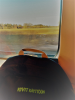 Musta Kyvyt käyttöön reppu junassa, taustalla peltomaisemaa.