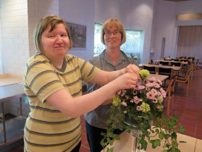 Hanna Pesonen hoitaa kukkia ja emäntä Arja Pikkarainen hymyilee taustalla.