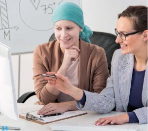 Kaksi naista tietokoneen näytön äärellä, toisella huivi pään peittona ja toinen tummatukkainen, joka opastaa.