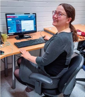 Viivi Kivelä harmaassa mekossa tietokoneen äärellä.