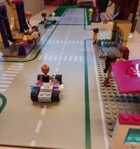 Legoelementti, jossa tie ja tiellä yksi legoukko autossa ja katselee kohti legokojuja kohti.