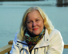 Ilse Vauhkonen valkeassa takissa jäässä olevan järven edessä.