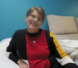 Hymyilevä Tiina Jäppinen musta, puna, keltaraidalisessa paidassa.
