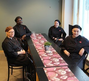 Tulevat ravintola-alan ammattilaiset tauolla tummissa työasuissaan pöydän ääressä.